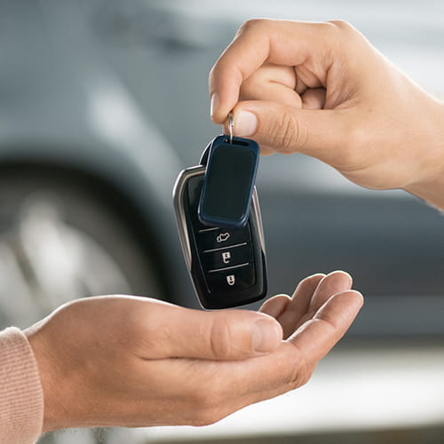 Someone handing a person a set of keys in a car dealership, tile card.