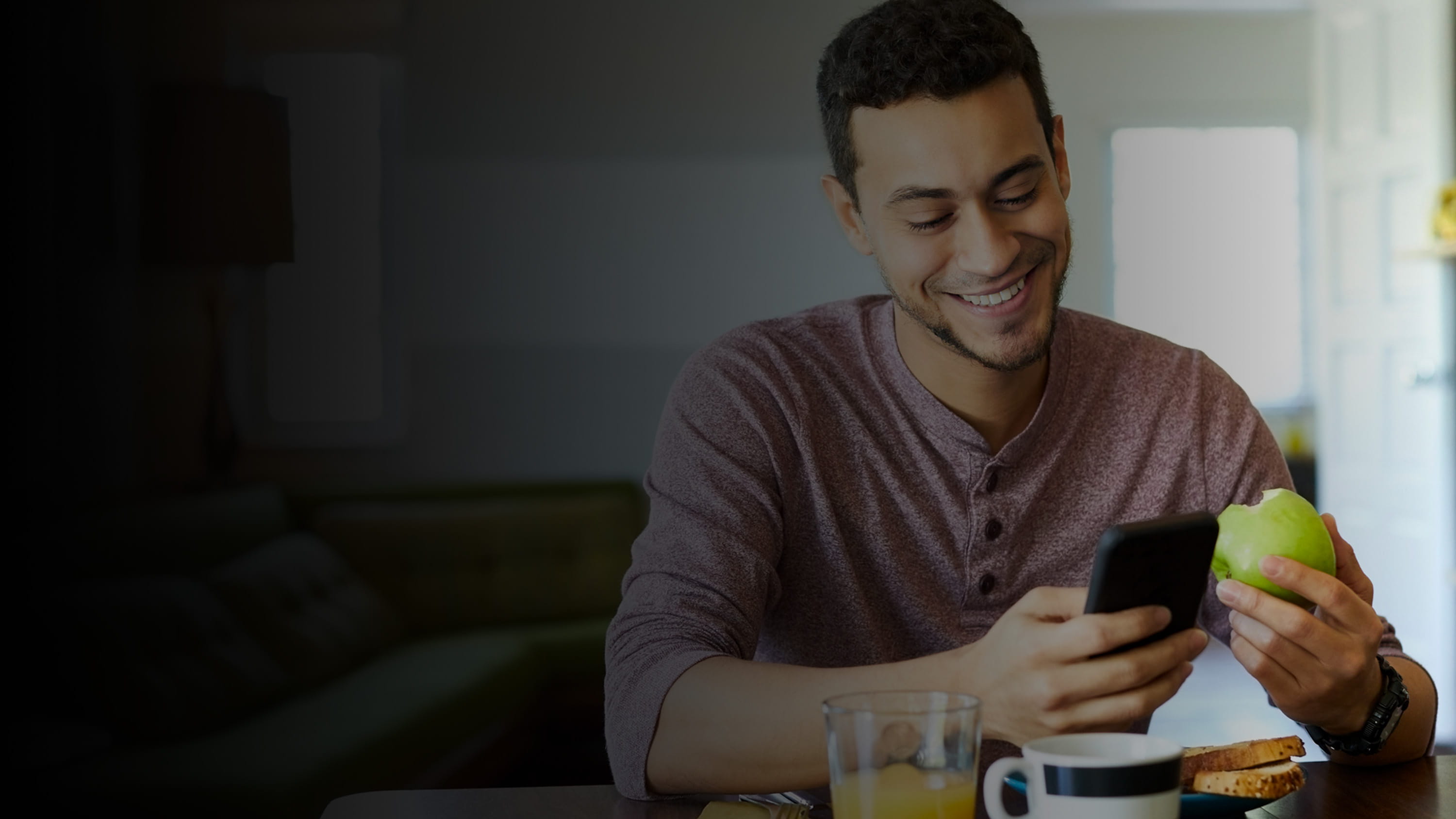 Man looking down at a cellular device and holding an apple.