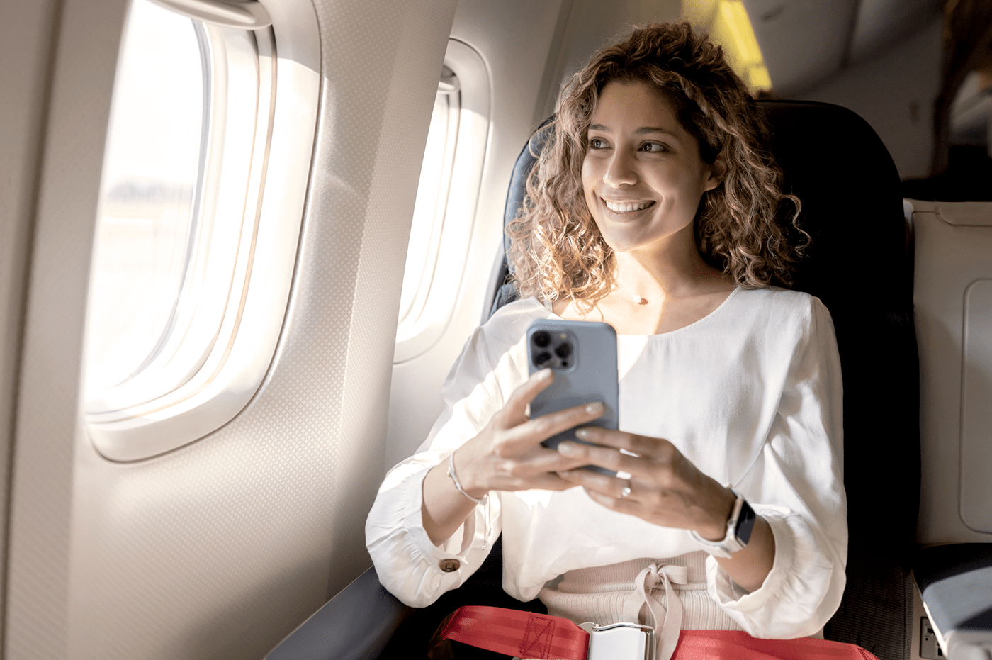 Woman sitting in an airplane seat looking out the window holding a cellular device