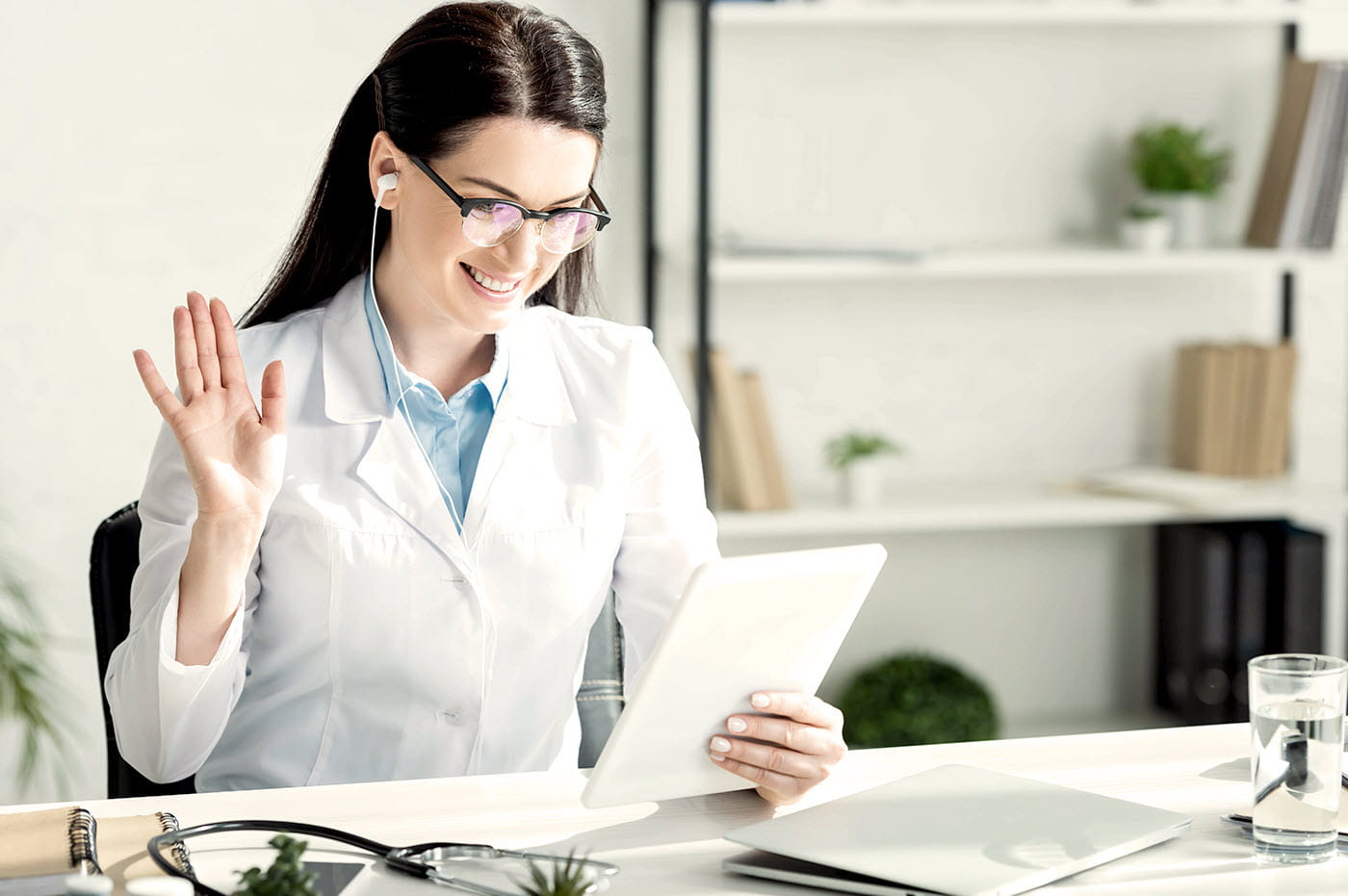 Female dentist waving to patient on iPad during a virtual appointment.