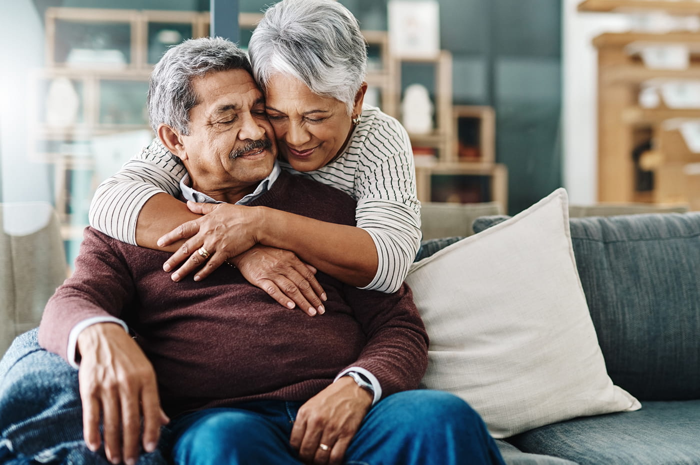 Older married couple sitting on couch and hugging.