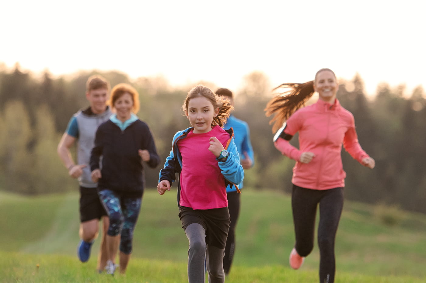 Some children and adults running together through a field in athletic clothes.