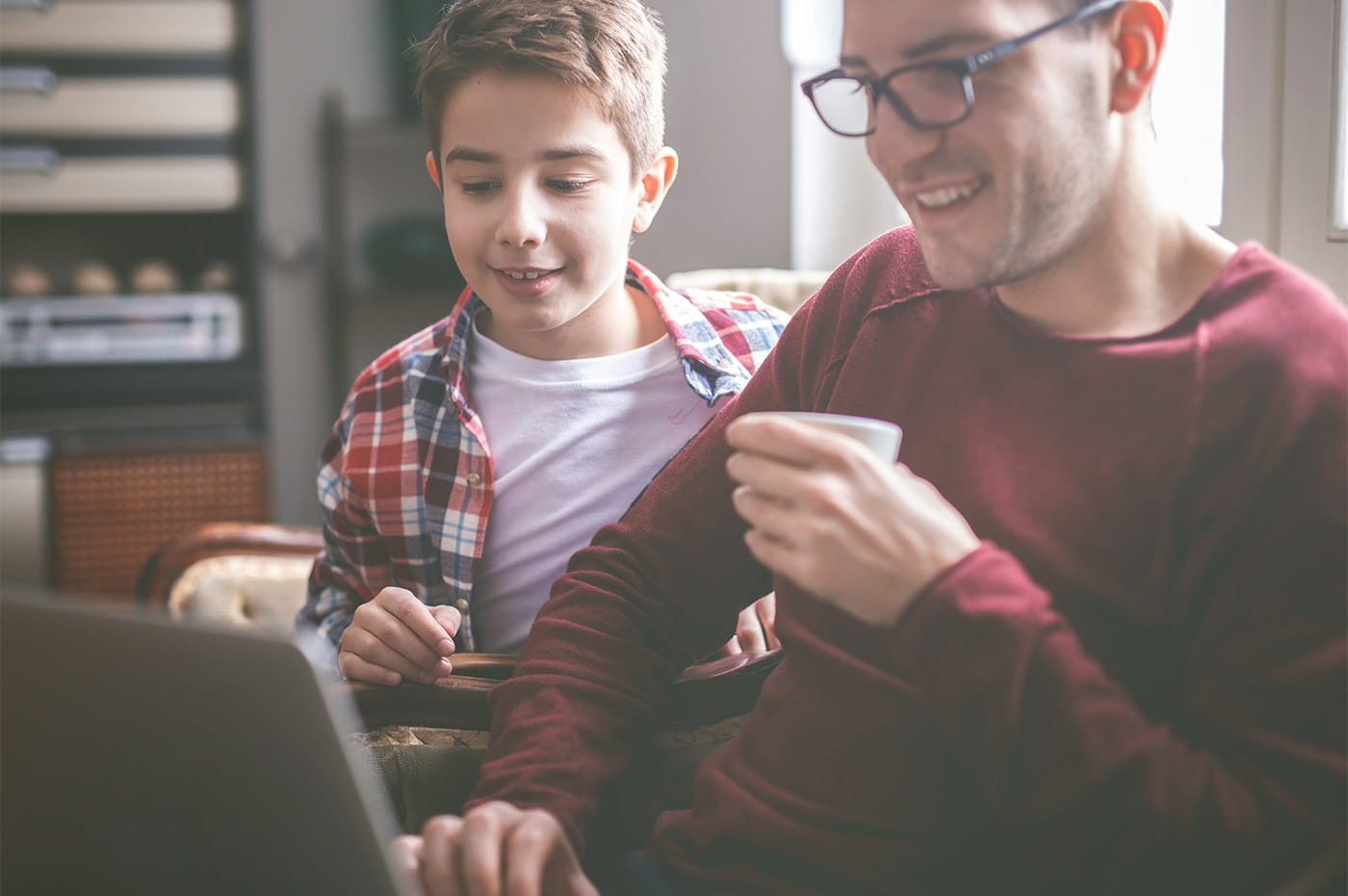 A white father and son sitting on the couch and looking at a laptop together.