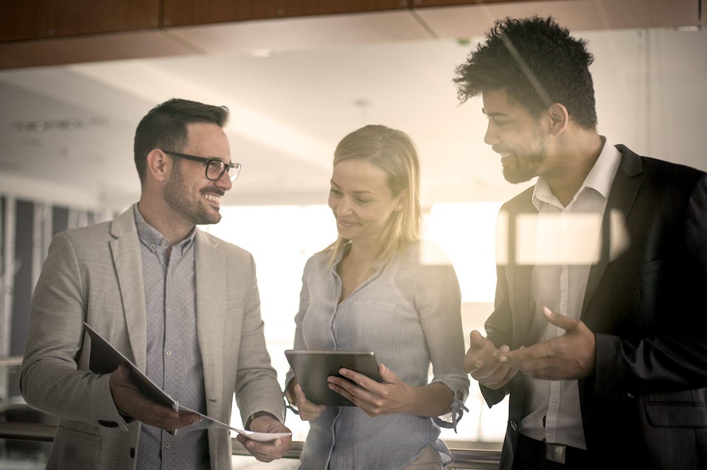 A group of coworkers talking to one another and all holding tablets in their hands. 