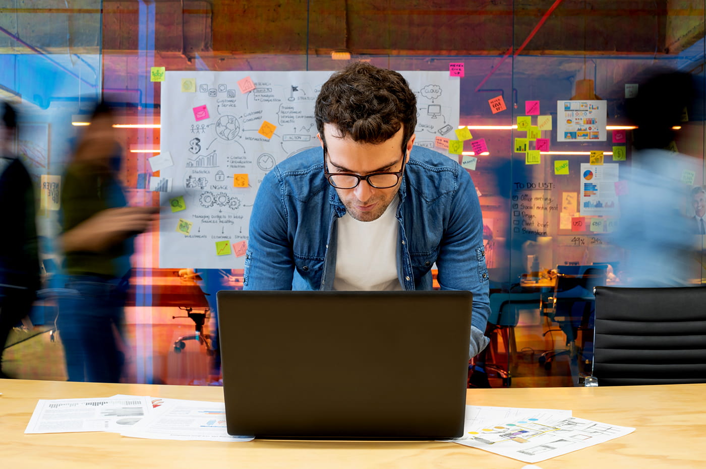 A man working on a laptop in a busy, fast-paced office.