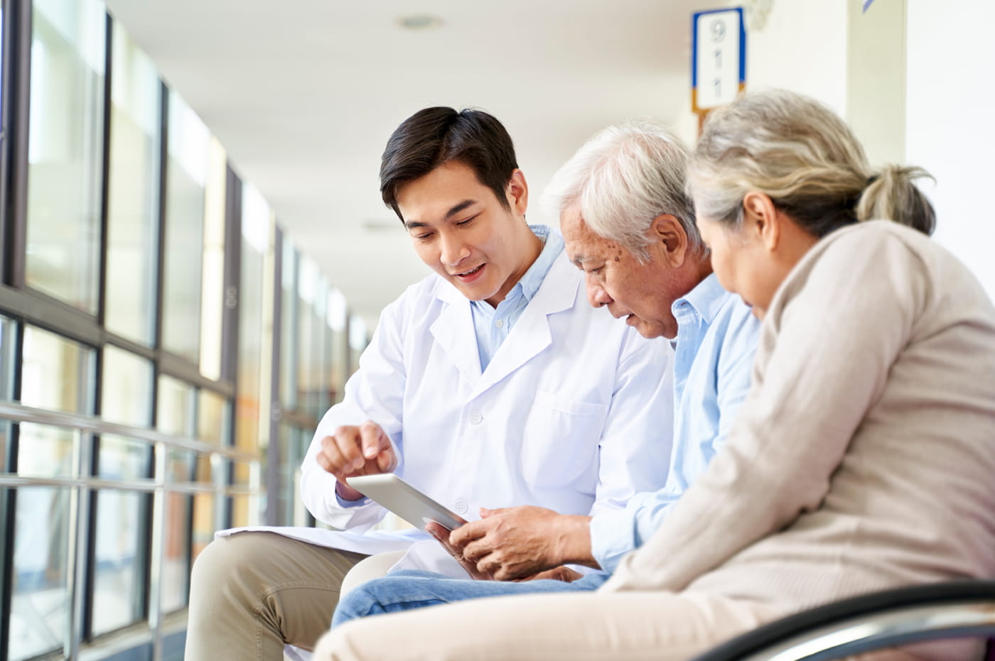 Younger male doctor talking with two older patients and looking at iPad.