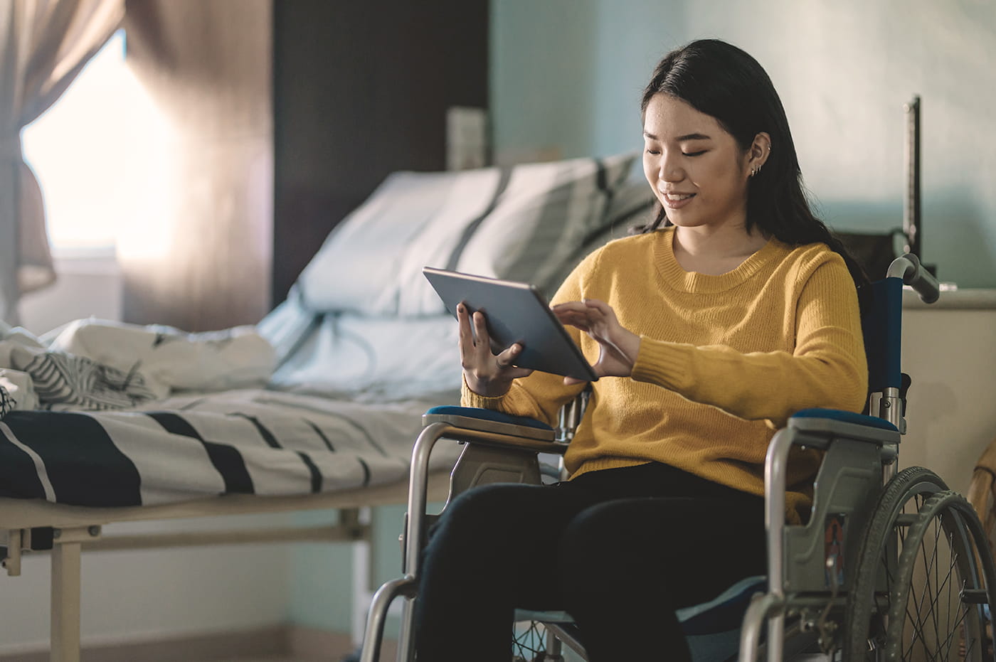 A young woman in a wheelchair working on a tablet.